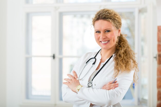 Молодая женщина-врач, стоя в клинике со стетоскопом на шее