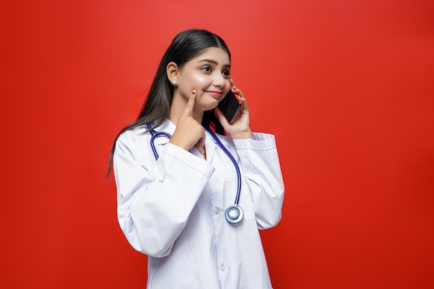 young female doctor talking on celphone with smile red background indian pakistani model