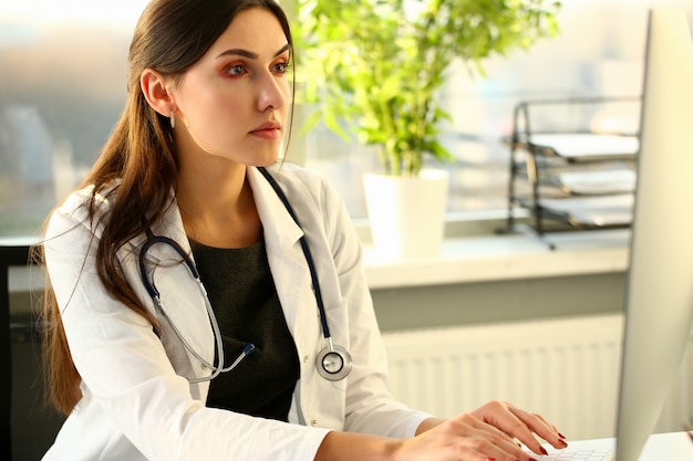 Young female doctor uses computer in workplace.