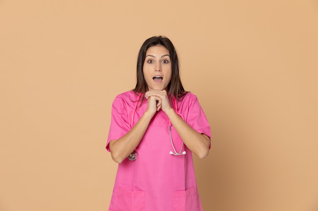 Young female doctor with a pink uniform gesturing over brown wall