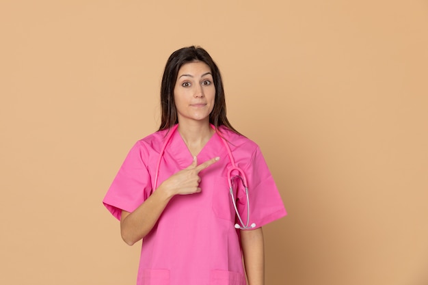 Young female doctor with a pink uniform gesturing over brown wall