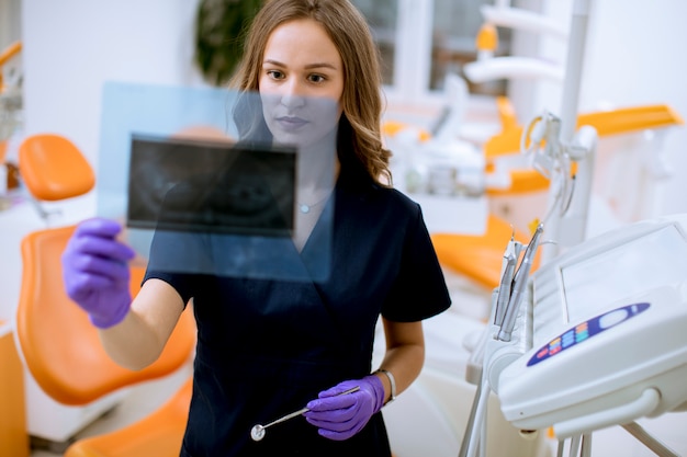 Фото Молодая женщина-врач с защитными перчатками, изучения рентгенограммы в офисе стоматолога