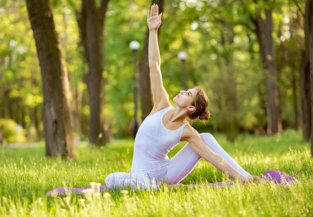 Молодая женщина делает йога стрейч и упражнения на траве в парке