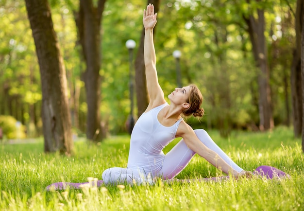 Young female doing yoga stretch and exercise on grass in the park