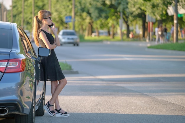 Young female driver standing near her car talking on mobile\
phone on a city street in summer