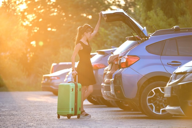 Young female driver taking out luggage suitcase bag out of her\
car travelling and vacations concept