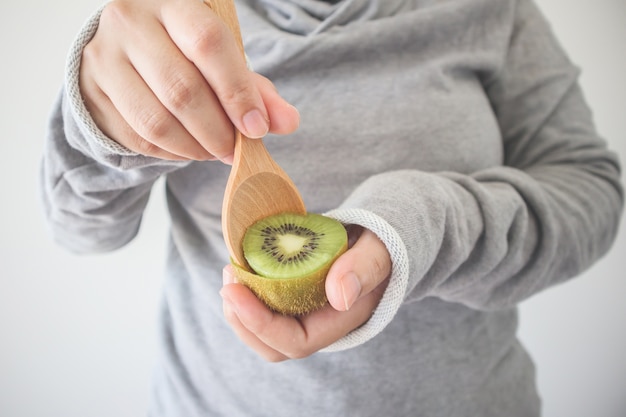 Giovane donna che mangia kiwi maturo con un cucchiaio di legno