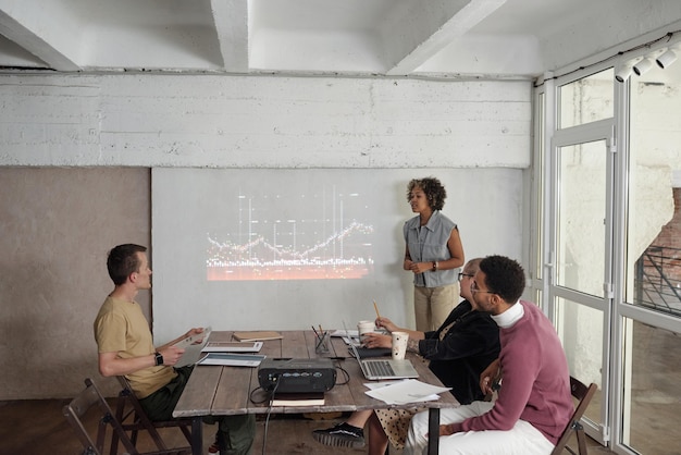 Young female economist standing by interactive whiteboard with financial graph