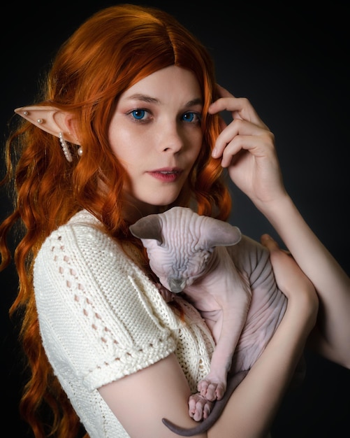 Young female elf cosplay with sleeping Sphinx kitten in hands Closeup portrait on black background