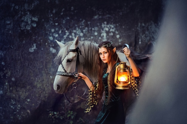 Foto giovane elfo femminile che cammina con il suo cavallo che tiene una lanterna