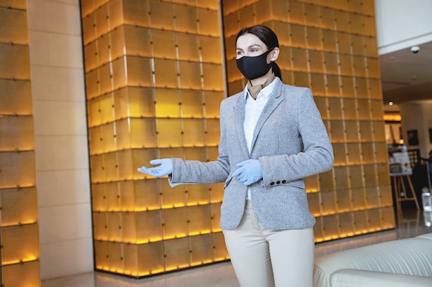 Young female employee wearing a mask and rubber gloves while showing the way to the rooms. website banner