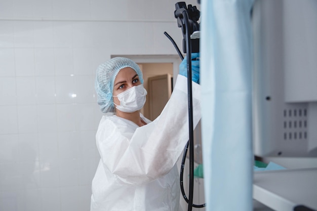 A young female endoscopist in a white protective suit cap and gloves prepares the equipment for work