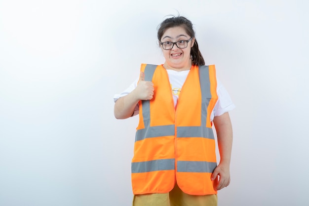 Young female engineer in glasses giving thumbs up on white wall