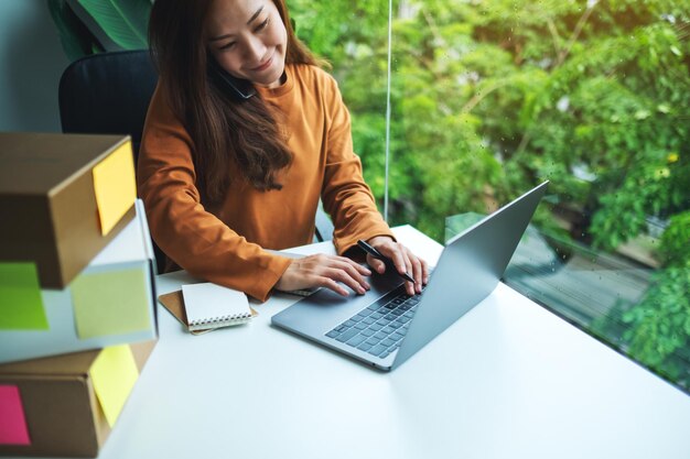 Young female entrepreneur confirming orders from customer on the phone and laptop for online shopping and delivery concept