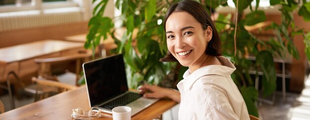 Photo young female entrepreneur girl sits with laptop in cafe works on remore from restaurant drinks