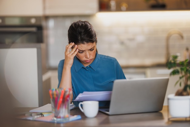 Young female entrepreneur looking stressed while working on laptop from her home office.