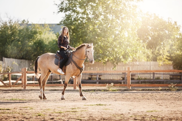 晴れた夏の日に牧場で馬に乗る若い女性の農場マネージャー