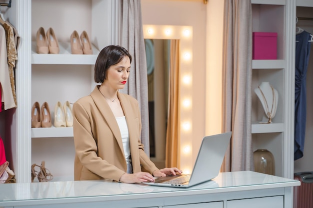 Foto giovane stilista femminile che effettua ordini online lavorando su laptop in studio donna su misura che consulta i clienti in remoto sul computer in officina piccola impresa