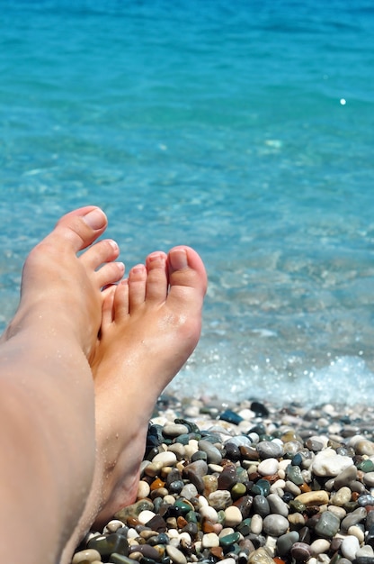 Photo young female feet on the beach with blue water