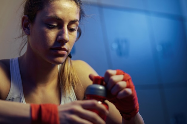 Молодая женщина-боец с бутылкой воды отдыхает в раздевалке спортзала