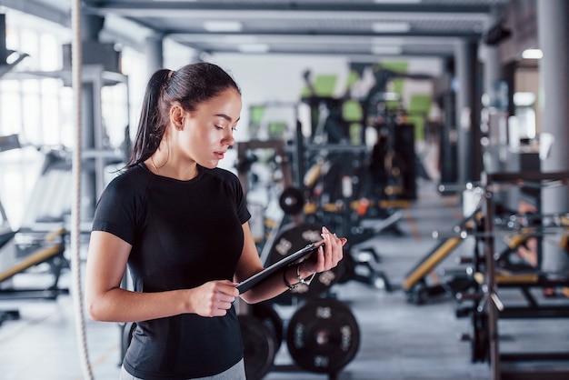 Istruttore personale di fitness femminile giovane con blocco note in piedi in palestra.