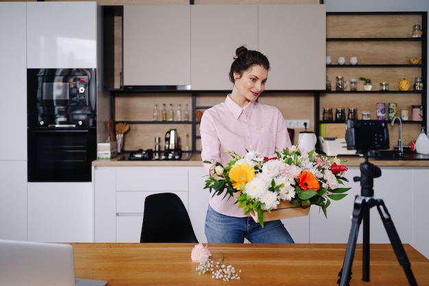 若い女性の花屋は、カメラで花の組成物のデザインのビデオチュートリアルを記録します女性のインテリアデザイナーは、カメラでvlogを撮影し、手作りの家の花の装飾をアレンジします