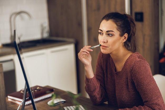 Young female freelance looking thoughtful while working on computer from her home office.