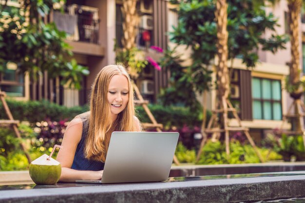 Young female freelancer sitting near the pool with her laptop. Busy at holidays. Distant work concept. Copy space for your text