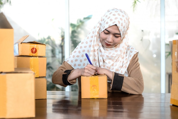 Young female freelancer wearing hijab writing on a box