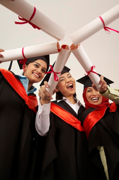 Photo young female friends holding degrees while standing against white background