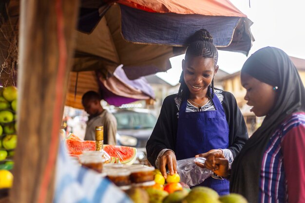 Photo young female fruit merchant on blue apron attending to buying client