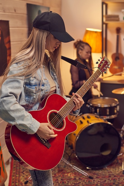 스튜디오에서 음악 그룹과 함께 일렉트릭 기타를 연주하는 젊은 여성 기타리스트