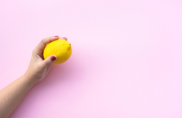 Young female hand holding lemon on pink pastel background.fruit and healthy concepts ideas