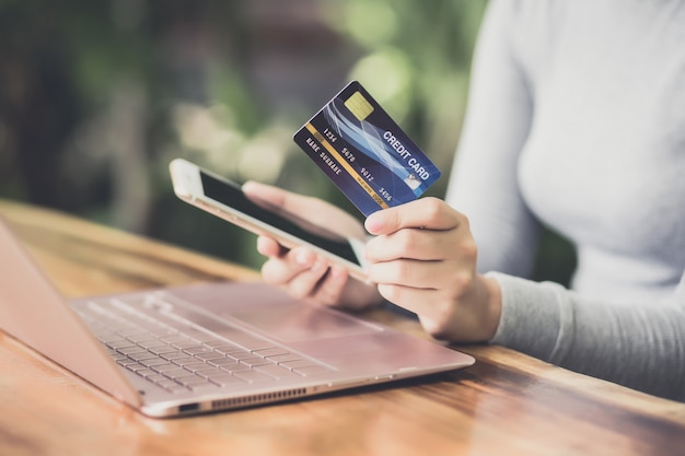 Young female hand holding plastic credit card and using laptop. Online shopping or paying concept.