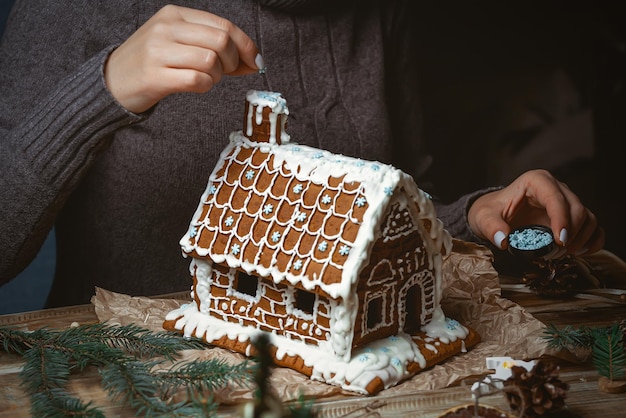 若い女性の手がクリスマスのジンジャーブレッドの家を飾る