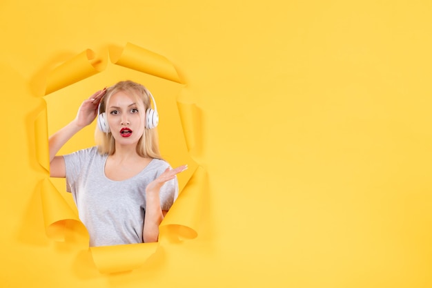 Young female in headphones on torn yellow paper background audio ultrasound sound music