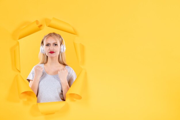 Young female in headphones on a torn yellow paper surface