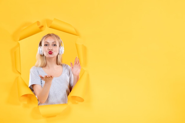 Young female in headphones on torn yellow paper surface