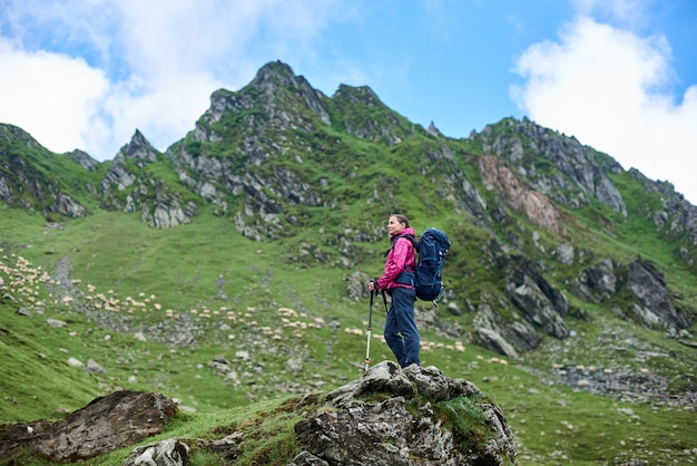 Giovane viandante femminile che gode di bella giornata di sole nelle montagne che riposano guardandosi intorno