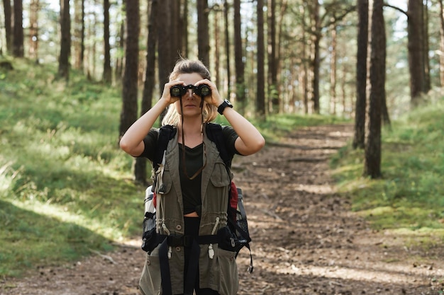 Young female hiker is using binoculars for bird watching in green forest