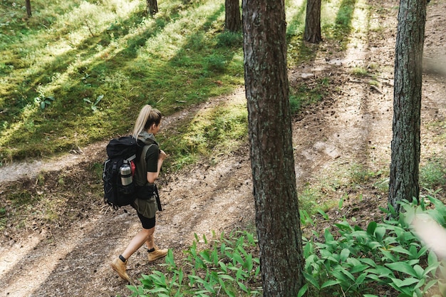 Young female hiker with big backpack in green forest