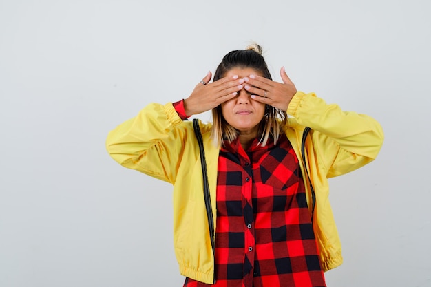 写真 市松模様のシャツを着た若い女性、手で目を覆い、焦点を合わせて見えるジャケット、正面図。