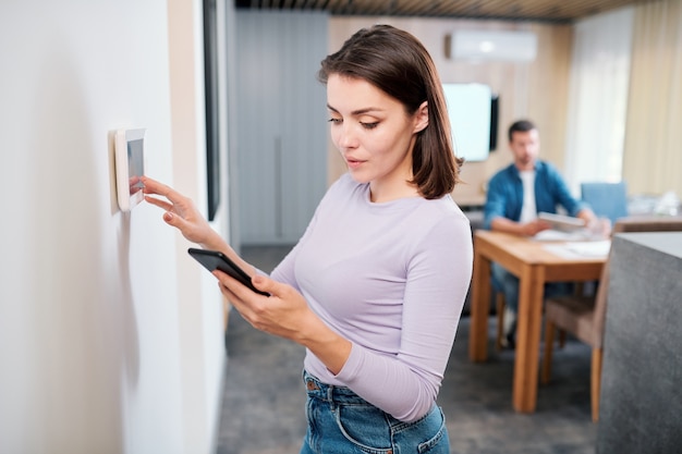 Young female installing new system of smart remote control in digital tablet hanging on the wall of living-room