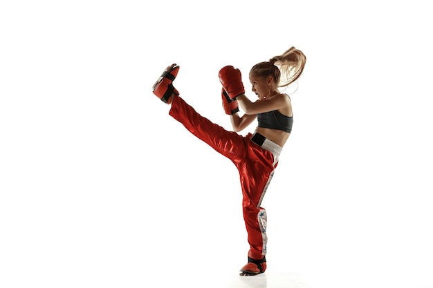 Молодая женская тренировка истребителя кикбоксинга изолированная на белой стене. Кавказская блондинка в красной спортивной одежде занимается боевыми искусствами. Понятие спорта, здорового образа жизни, движения, действий, молодежи.