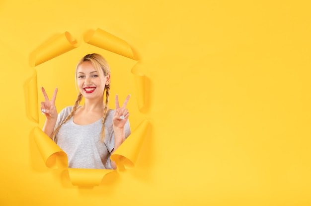 Young female looking from torn yellow paper background indoor facial window