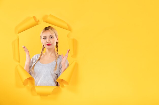 Young female looking from a torn yellow paper background window indoor sale facial