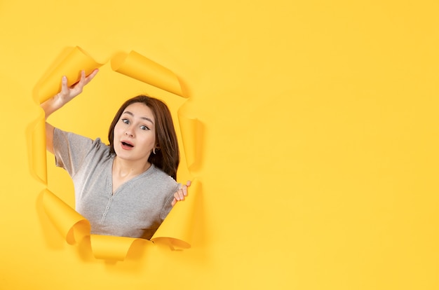 young female looking through a hole in a yellow paper surface window advertising look