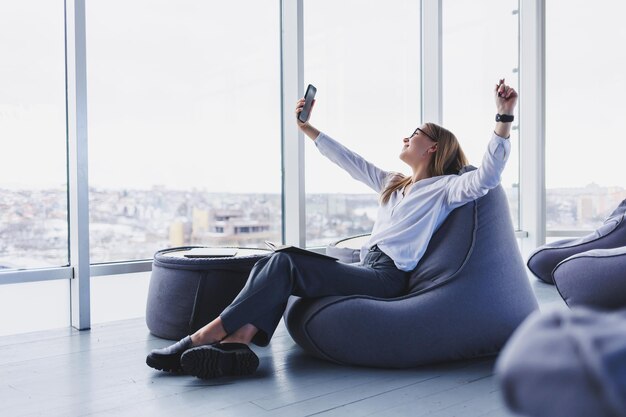 Young female manager in glasses sits on a soft pouf after a working day modern workspace in the office