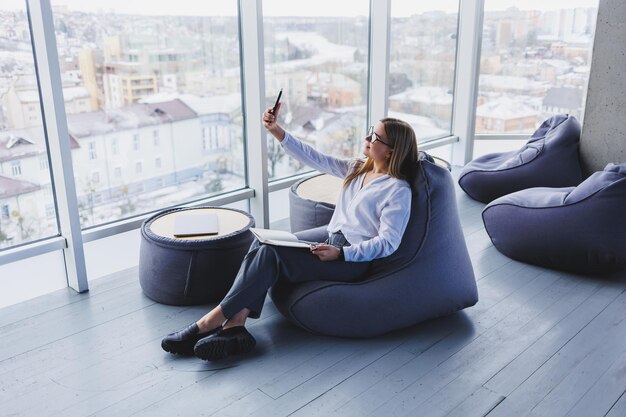 Young female manager in glasses sits on a soft pouf after a working day modern workspace in the office