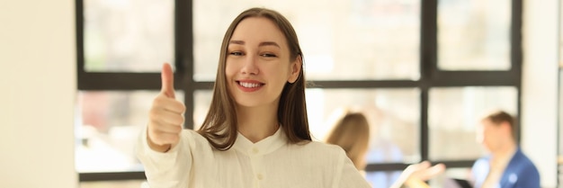 若い女性マネージャーが笑顔でオフィスで親指を立て、良いフィードバックとコンセプトを示す